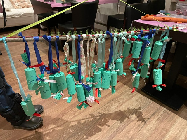 Selbstgebastelter Adventskalender aus, mit grünem Krepppapier verpackten und beschrifteten, Toilettenpapier-Rollen
