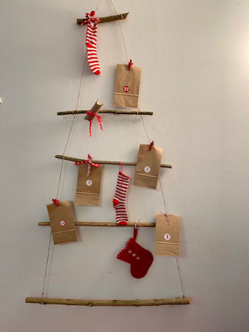 Adventskalender komplett Ein selbstgemachter Adventskalender in Form eines Tannenbaums aus Holzstäben und Schnüren, der mit Tütchen und roten Stümpfchen bestückt ist.