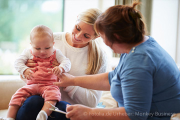 Bild von einer jungen Mutter mit ihrem Baby auf dem Schoß auf einem Sofa neben einer älteren Frau