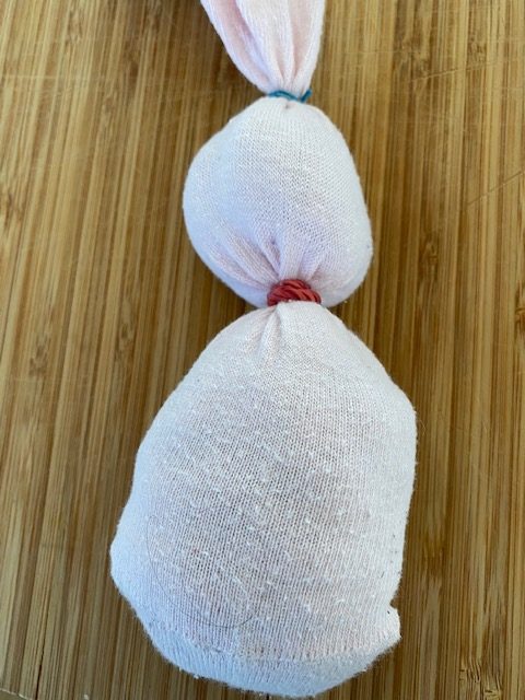 2. Bastelschritt für die Umsetzung einer Osterhasen-Figur: Eine mit Watte gefüllte weiße Socke, ist an zwei Stellen mit Kordeln so zugebunden, dass die Socke die Figur eines Hasen vermuten lässt.