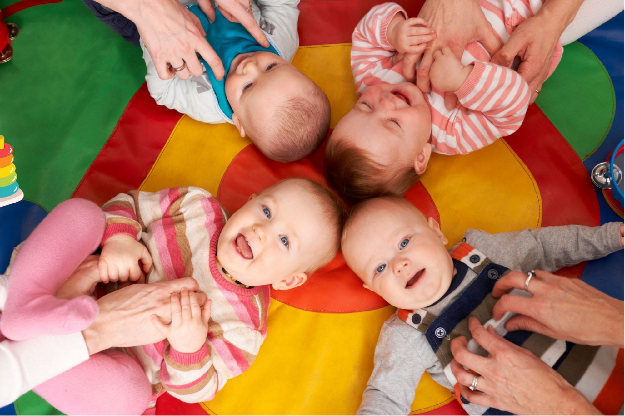 Kinder liegen im Kreis auf einer Spieldecke. Es sind auch Hände der dahintersitzenden Eltern zu sehen.